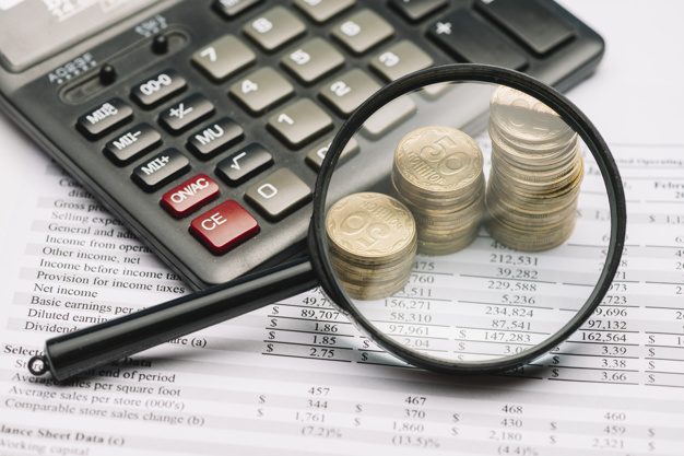 Magnifying glass over the coin stack and calculator on financial report Free Photo
